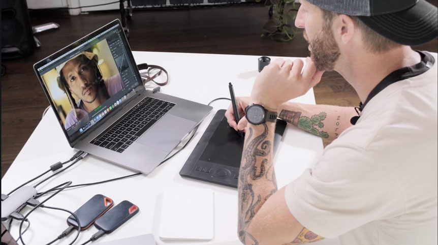 Tattooed photographer editing images with tablet and laptop
