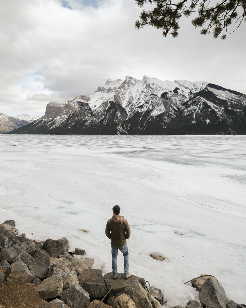 Man looking out over frozen lake with mountains in background