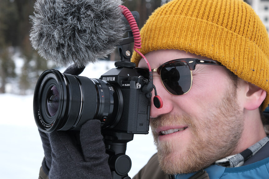 Close-up of man in wooly hat and sunglasses holding FUJIFILM X-S20 camera to his eye