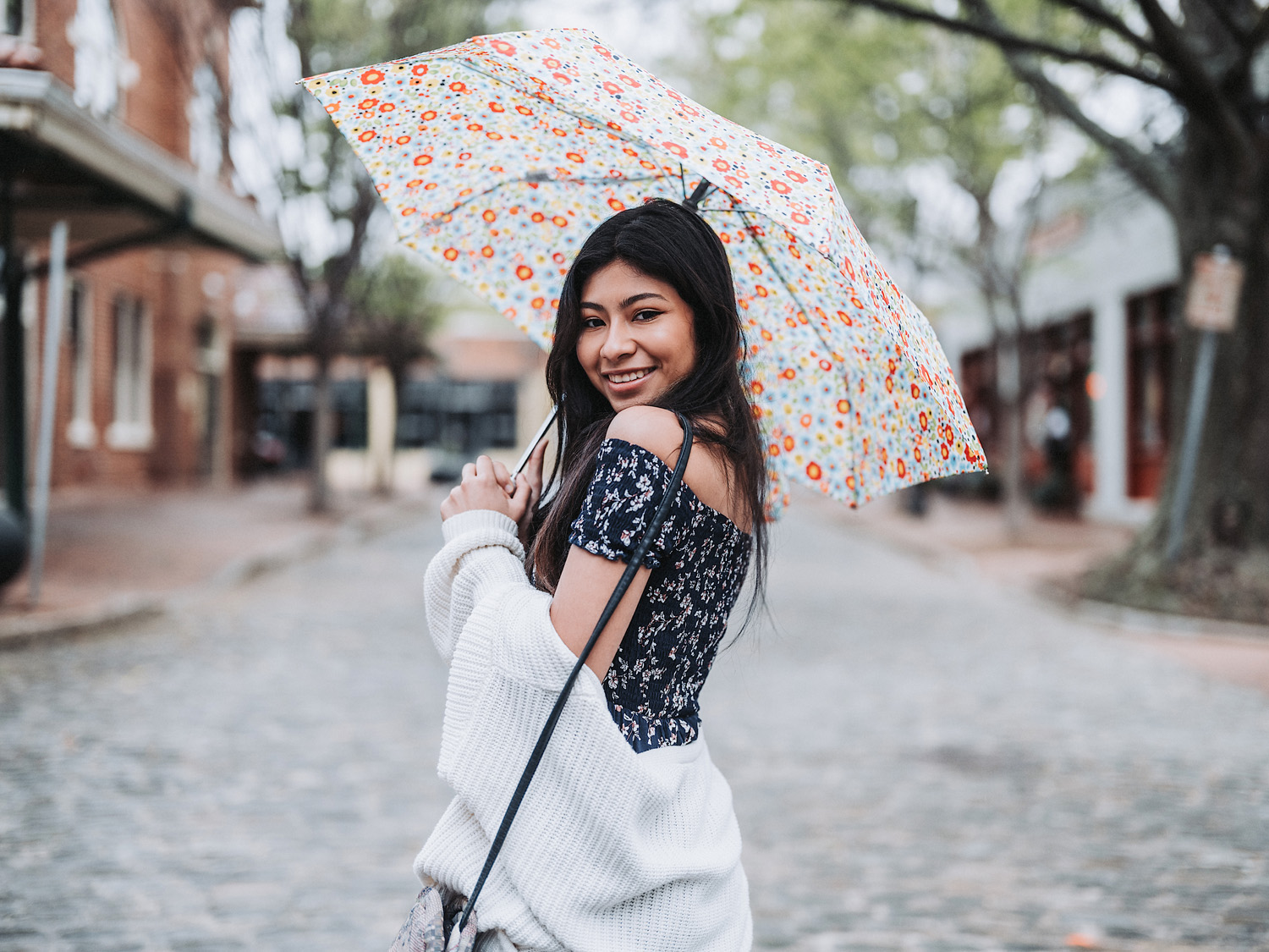 Woman with black long hair smiling and holding floral umbrella