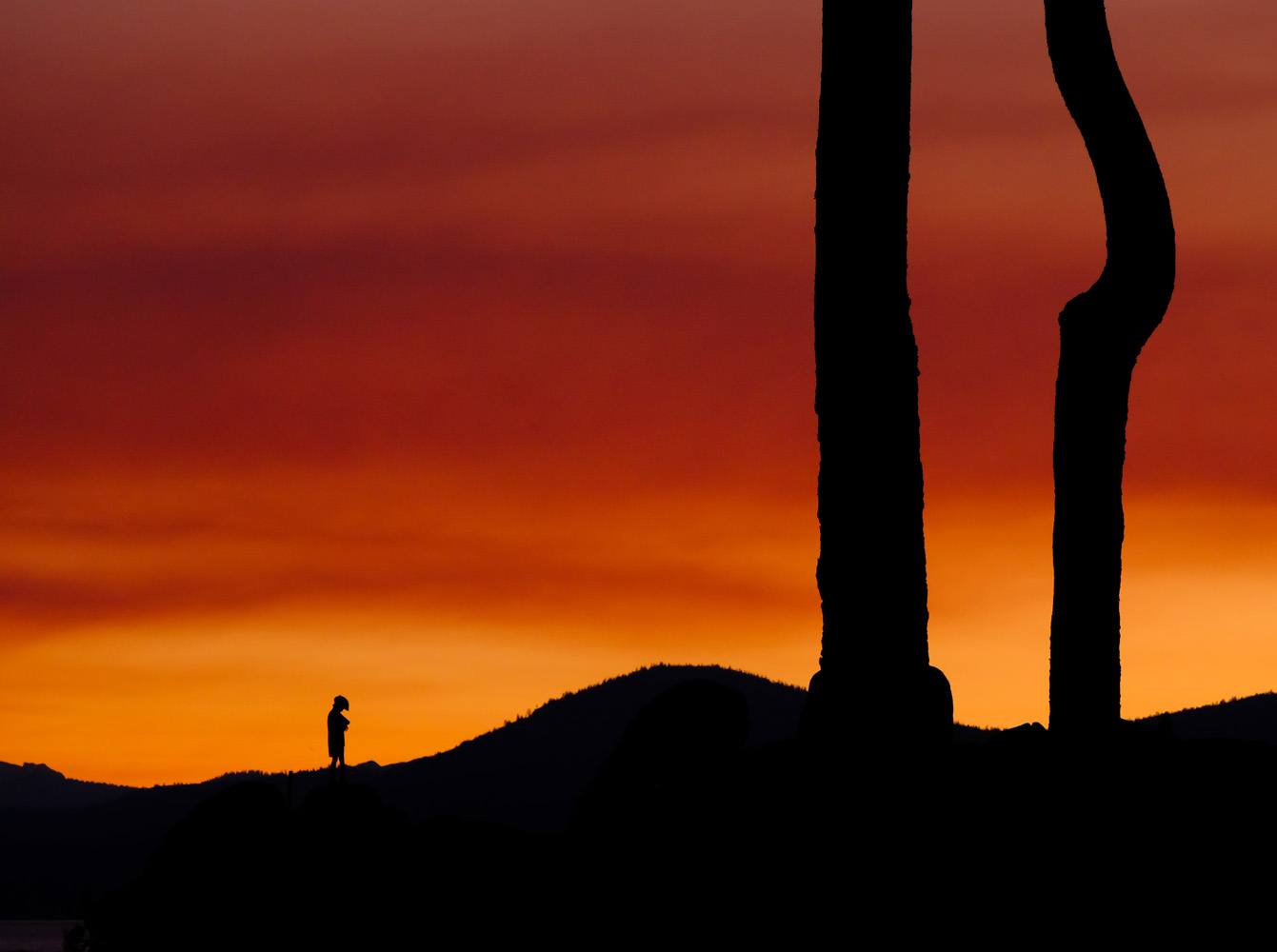 telephoto image of silhouetted person standing on horizon at sunset.