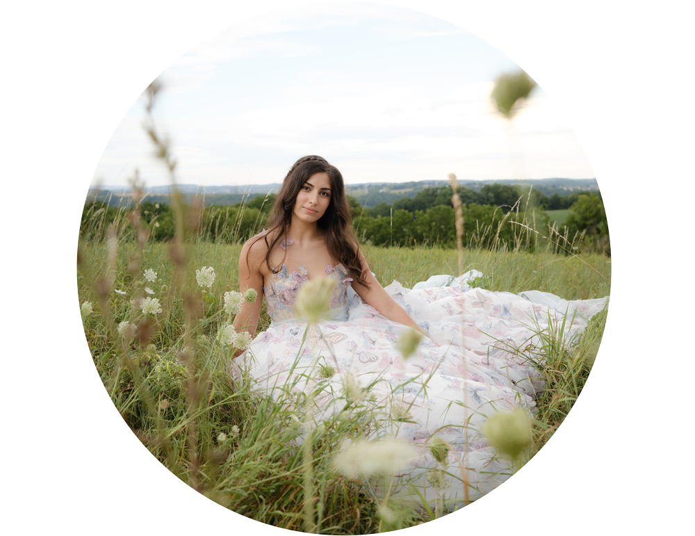 Bride sitting in summer meadow surrounded by long grass and wildflowers. Circular crop