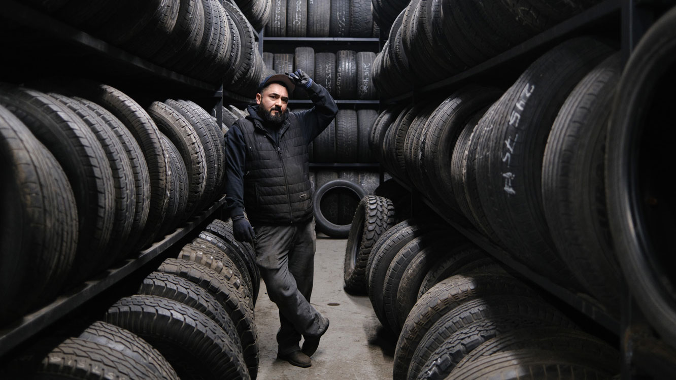 mechanic standing in workshop between racks of car tyres