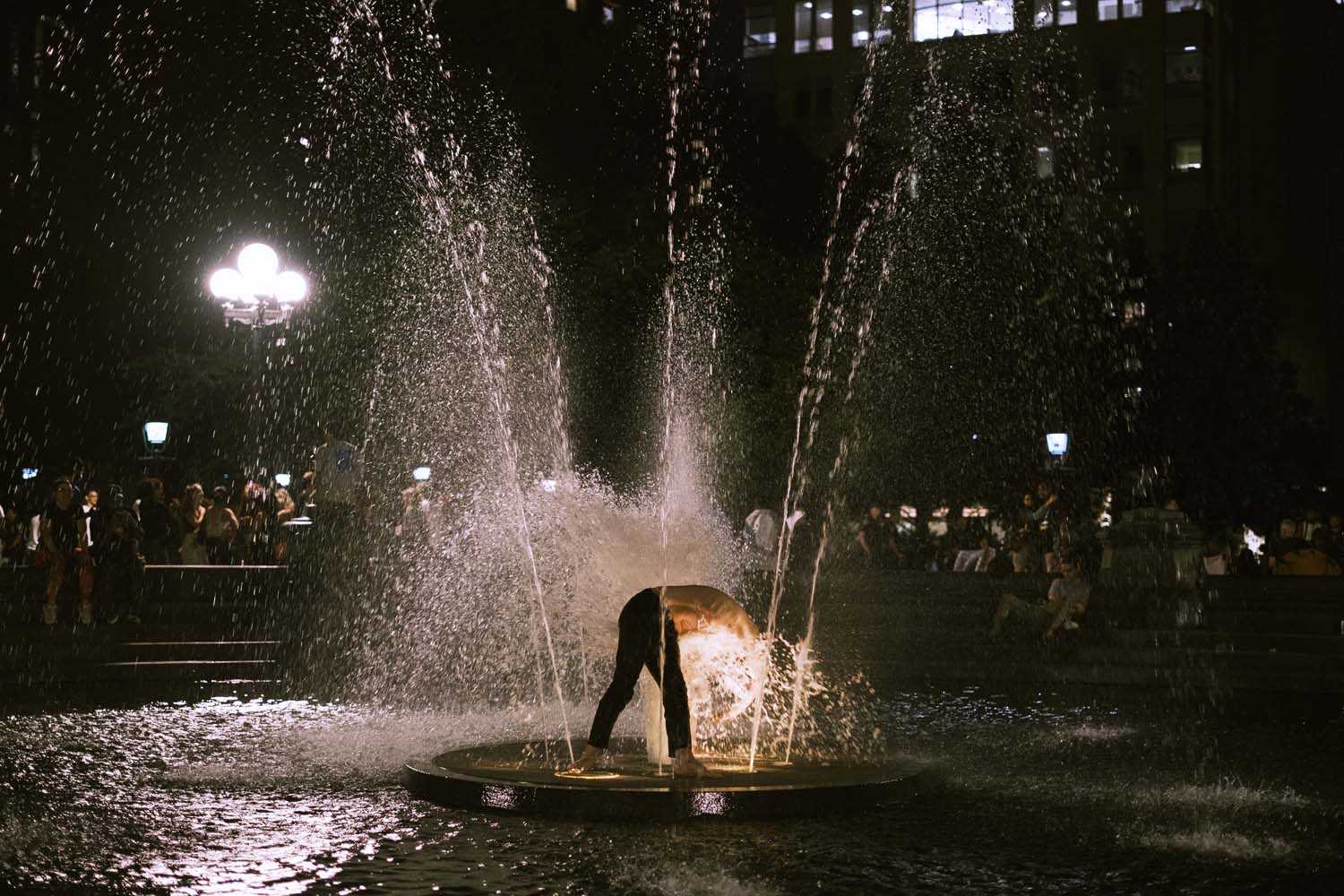 Shirtless man standing in New York City fountain with his head in a jet of water