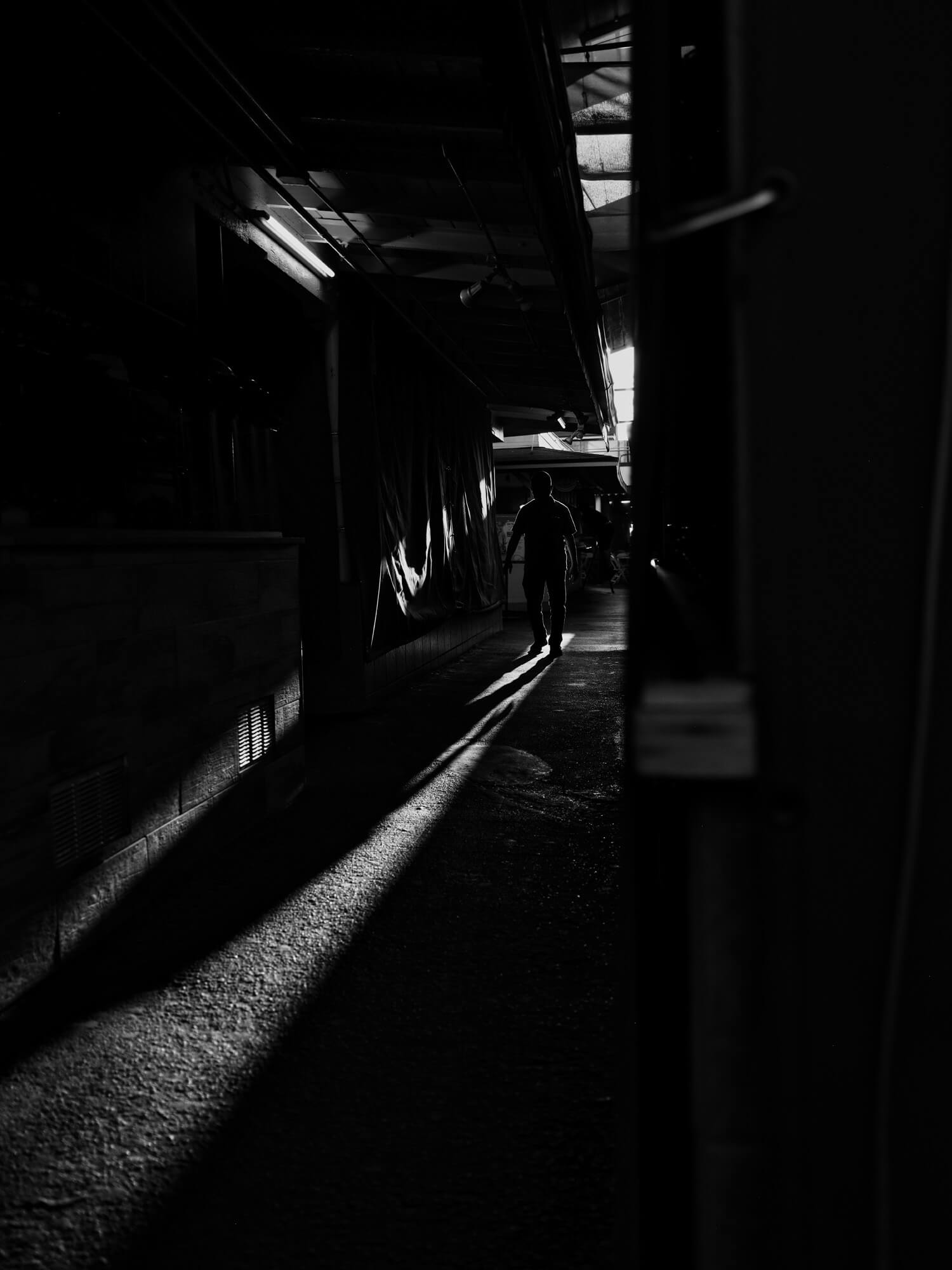 Silhouette of man standing at the end of a shadowy alleyway