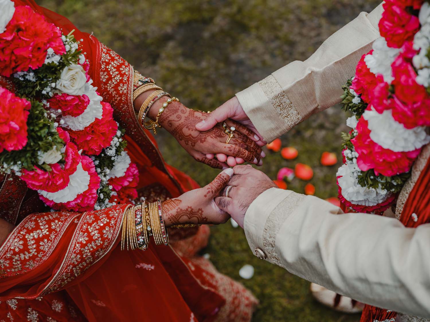 An Indian couple hold hands during their elopement, highlighting henna, dress detail, jewellery and flowers