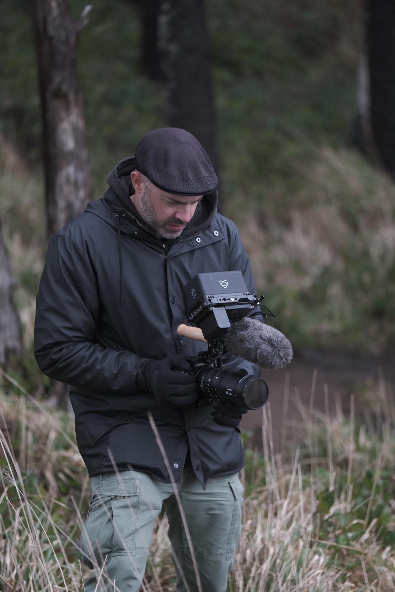 A man in a raincoat aims his camera at something out of frame